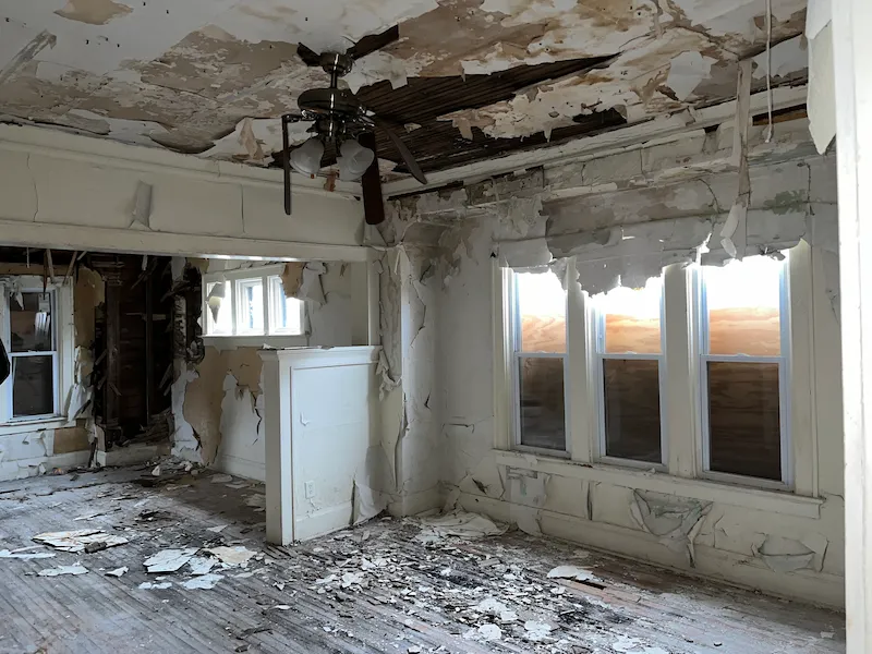 Old interior room with white walls, floor removed, and ceiling falling in