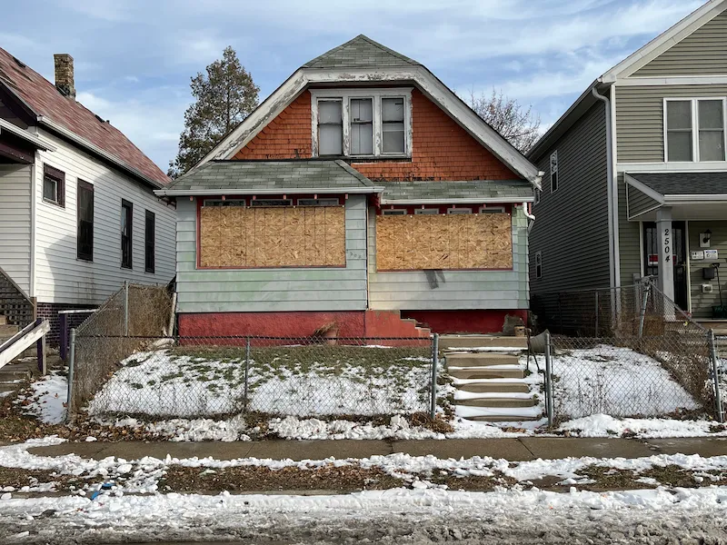 Old orange boarded up house with gate and sloped roof